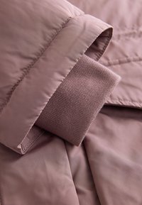 Gros plan d'une manche de veste matelassée rose avec un poignet en maille côtelée s'étendant de l'intérieur du tissu extérieur.