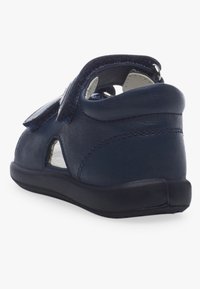 Chaussure en cuir marine avec un dos arrondi, des côtés ouverts et une bande Velcro. Comprend une semelle en caoutchouc noir et des accents de couture minimalistes.