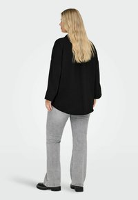 Črna dolga majica z raztegnjenim krojem in detajlom pregiba na hrbtu, kombinirana s svetlo sivimi širokimi kavbojkami in črnimi platformnimi škornji.