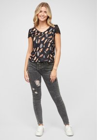 Haut noir à manches courtes avec imprimé plumes, accents en dentelle sur les manches. Jeans skinny gris clair avec détails déchirés, associés à des baskets blanches.