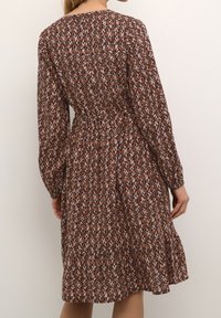 Vestido marrón con estampado que presenta mangas largas, una cintura ceñida y una falda acampanada con un diseño geométrico en tonos crema y óxido.