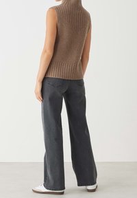Brauner, ärmelloser Strickpullover mit Rippenstruktur und hohem Kragen, kombiniert mit weitem grauem Jeans und weißen Turnschuhen.