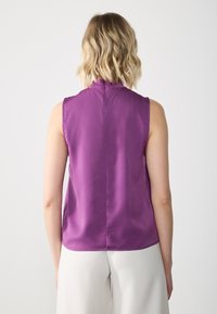Lilla sateng topp uten ermer med høy hals. Smooth tekstur, glidelås bak og en litt buet kant. Designet for en tettsittende passform.