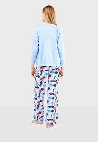 Sudadera azul clara de manga larga, combinada con pantalones de pijama con un patrón de formas abstractas en rojo, azul y negro sobre un fondo blanco.