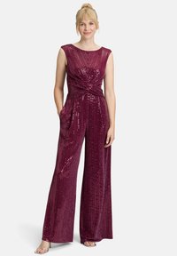 Combinaison bustier bordeaux ornée de sequins, avec un détail enroulé sur le devant, des pantalons à jambes larges et des poches latérales, associée à des talons argentés.