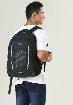 Zaino nero con dettagli verde chiaro, tasche in rete e design a corda elastica sulla parte frontale. Spallacci imbottiti per un maggiore comfort.
