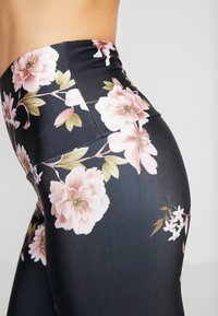 Bloemleggings met een zwarte achtergrond, voorzien van grote roze bloemen en groene bladeren, met een gladde textuur, hoge tailleband en een aansluitend ontwerp.