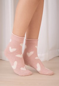 Pink socks with white heart patterns, made from a soft, knitted material. Ankle length with ribbed cuffs and seamless toe construction.