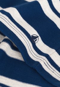 Marineblau und cremegestreifter Stoff mit glatter Textur, der ein kleines gesticktes Logo in der Nähe des Randes aufweist.