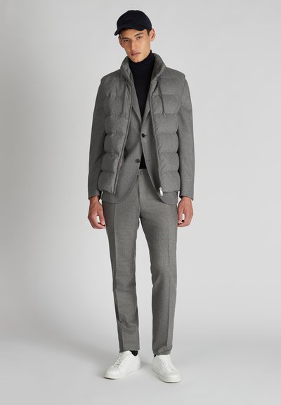 Szary kamizelka puchowa na dopasowanym garniturze, z wysokim kołnierzem, przednimi kieszeniami i subtelną teksturą. Połączona z białymi sneakersami.