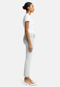 Jean in denim chiaro con vestibilità dritta, orlo sfrangiato, abbinati a tacchi slingback bianchi con punta e una t-shirt bianca aderente.