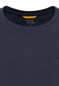 Marineblå bomulds t-shirt med rund hals. Har en gul detalje ved kraven og et lille logo på forsiden. Størrelse L.
