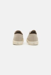Beige canvas sneakers with a textured finish, featuring a rubber sole, rear logo accent, and simple lace-up design.