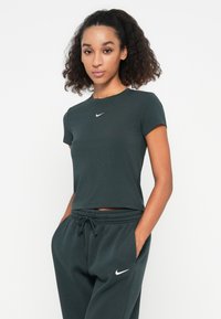 Trumpas rankovėmis, tamsiai žalias marškinėliai iš minkštos, tamprios medžiagos su apvaliu kaklu, su mažuoju baltu Nike logotipu krūtinėje.
