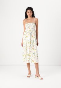 Λουλουδάτο μίντι φόρεμα με σμιλευμένο κορσάζ, λεπτές τιράντες και ζωντανά πολύχρωμα σχέδια σε λευκό φόντο. Απαλό και ελαφρύ ύφασμα.