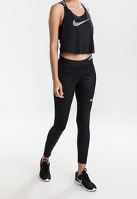 Černý crop top Nike s logem, doplněný černými legínami s texturovaným vzorem. Dokončeno černými sportovními botami.