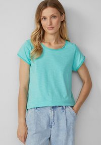 T-shirt court à manches courtes de couleur bleu-vert clair avec un col rond et une coupe décontractée. Texture douce, motif chiné subtil et poignets de manches retroussés.