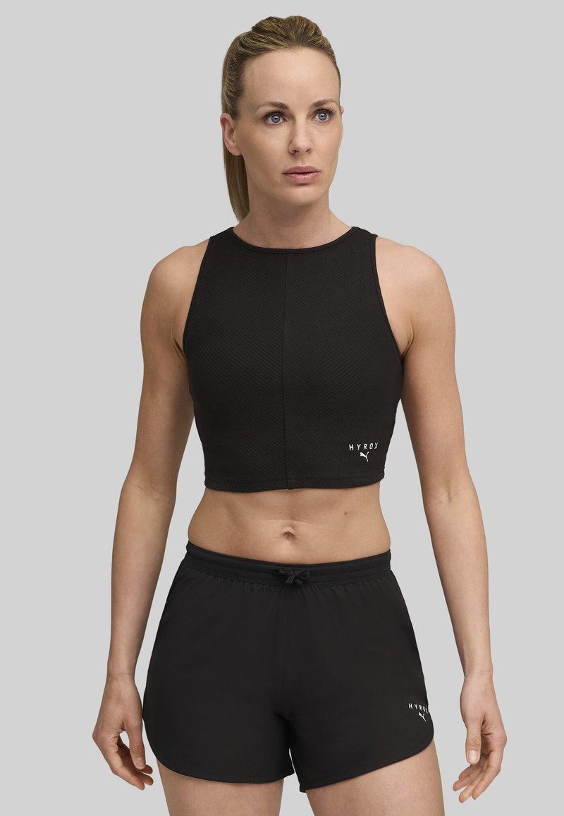 Sort atletisk crop top med tekstureret materiale, høj halsudskæring og logo-detalje, parret med sorte shorts med elastisk talje og snøre.