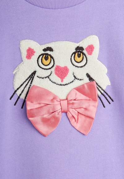 Lilla genser med en brodert hvit katteansikt med gule øyne, rosa kinn og en rosa satengsløyfe. Strukturell og leken design.