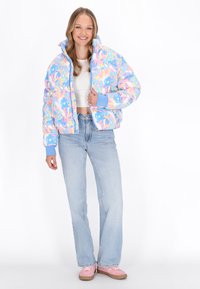 Barevná péřová bunda v pastelově modré barvě s abstraktními vzory. Obsahuje vysoký límec a žebrované manžety. V kombinaci se světlomodrými džíny a růžovými botami.