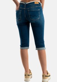 Pantalons capri en denim bleu foncé avec des revers, présentant un détail au niveau de la taille et deux poches arrière avec de simples motifs de couture.