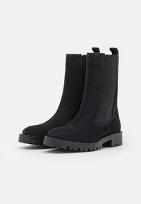 Black suede Chelsea boots with chunky rubber soles, elastic side panels, and pull tabs on a white background.