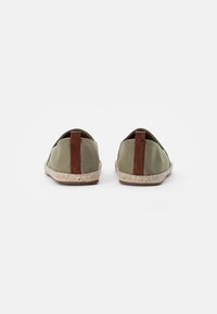 Gröna kanvas slip-on skor med bruna läderdetaljer, elastiska sidopaneler och vävda rep-sålar, som visar upp en minimalistisk design.