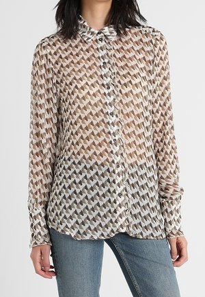 Chemise transparente à boutons présentant un motif géométrique marron et crème, à manches longues et avec un col classique. Associée à un jean bleu.