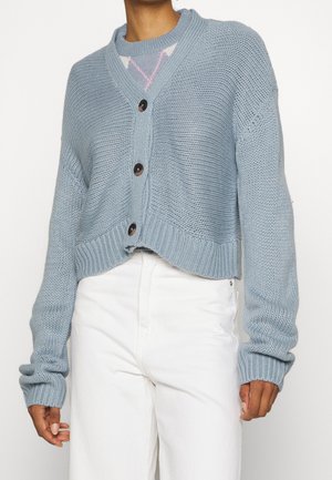 Cardigan court bleu clair en tricot texturé, avec un devant boutonné, des poignets côtelés et un design en v-neck avec des accents contrastés.
