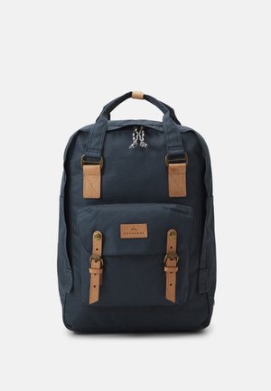 Sac à dos bleu foncé avec poche avant, deux sangles en cuir marron clair avec boucles, et deux poignées en haut sur un fond uni.