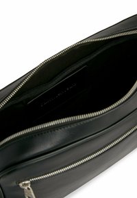 Interno di una borsa in pelle nera con una texture liscia, chiusura a zip e una patch etichetta. Presenta un design semplice e elegante senza dettagli extra.