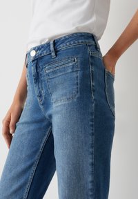 Blauwe denim jeans met een aansluitend ontwerp, met een vlakke voorkant, twee achterzakken en een zilveren knoopsluiting bij de taille.