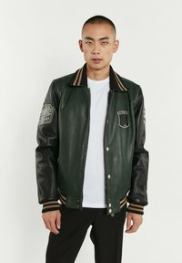 Veste varsity en cuir vert avec des manches en cuir noir, col et poignets côtelés rayés, patches brodés et fermeture éclair.