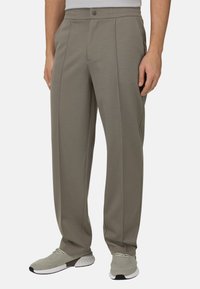 Pantalon gris clair sur mesure avec une texture lisse, doté d'un devant plat, de poches latérales et d'une ceinture élastique. Associé à des baskets grises.