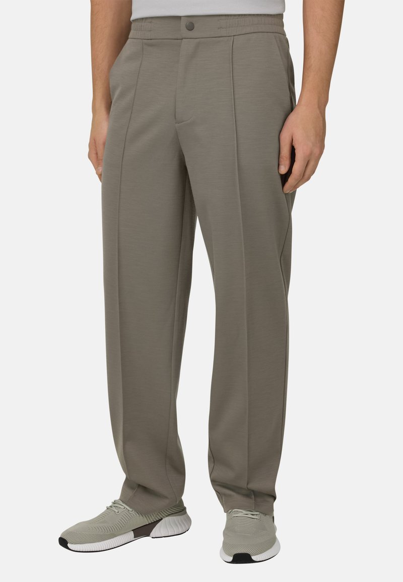 Pantalon gris clair sur mesure avec une texture lisse, doté d'un devant plat, de poches latérales et d'une ceinture élastique. Associé à des baskets grises.