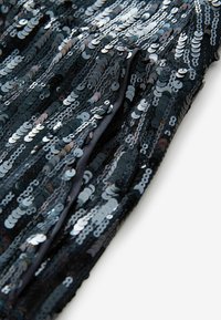Tissu noir densément couvert de sequins noirs et argentés brillants disposés en rangées verticales sur une surface lisse.