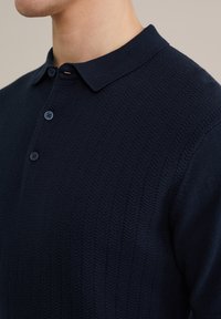 Polo shirt de punto en azul marino con un patrón texturizado de espiga, con un cuello clásico y una tapeta de tres botones. Puños suaves y acanalados.