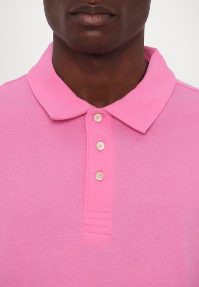 Polo rose avec un col, trois boutons à l'avant et des manches courtes. Texture lisse avec des détails de couture simples.