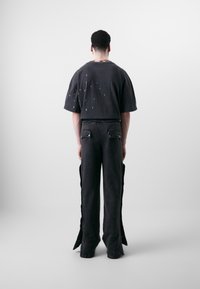Sort oversized t-shirt med sølvnitter på ryggen, parret med sorte bukser med vide ben, som har siderift og to baglommer.