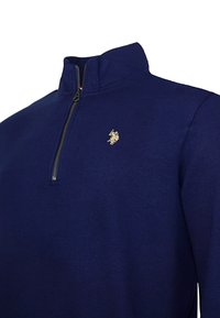 Navy blue quarter-zip pullover made of soft cotton blend, featuring a gold emblem on the chest and a smooth texture.