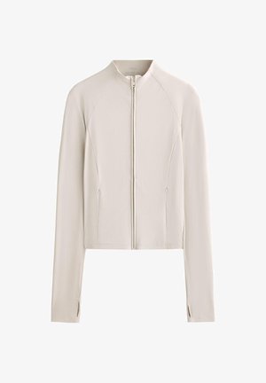 Veste cropped beige clair avec un col montant, fermeture éclair frontale complète, manches longues et poches zippées sur les côtés. Tissu lisse et extensible avec un minimum de détails de couture.