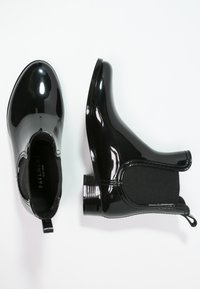 Bottines noires imperméables jusqu'à la cheville avec une finition brillante, des panneaux latéraux élastiques et un talon texturé. Comprend une languette pour un enfilage facile.