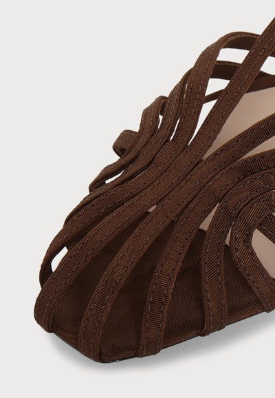 Gros plan d'une sandale marron avec plusieurs fines lanières texturées croisant le pied et un design à bout ouvert.