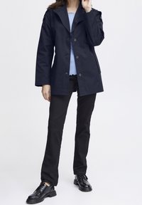 Námorně modrý kabát s špičatým límcem, předním zapínáním na knoflíky a bočními kapsami, spárovaný se světle modrým topem, černými kalhotami a černými šněrovacími botami.