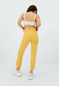 Gula högmidjade jeans med smal ben, femfickdesign och lätt textur, kombinerat med en vit ribbad crop top och sneakers.