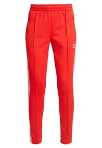 Röda träningsoverallsbyxor med elastisk midja, sidofickor med dragkedja och kontrasterande vita ränder längs sidorna. Tillverkade av mjukt material.