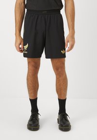 Fekete sportnadrág arany díszítéssel, sas mintával és "Mexikó" felirattal. Rugalmas derékpánttal és sima szövettextúrával.