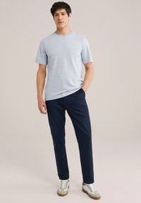 T-shirt a righe blu chiaro, maniche corte, collo tondo classico; abbinato a pantaloni blu scuro e scarpe sportive bicolori con accentuazioni bianche e color tan.