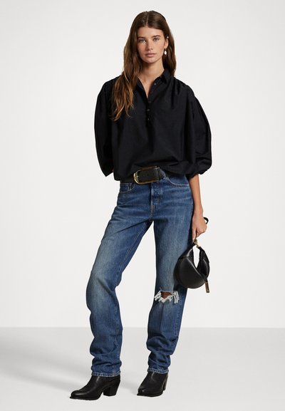 Svart oversized skjorte med knappestolpe, parret med løse blå jeans med slitte detaljer. Svarte ankelstøvler og liten håndveske.