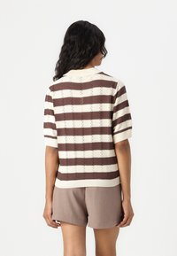 Strikket kortermet genser med vekslende brune og kremfargede striper, ribbestrikket krage og intrikat teksturdetalj.